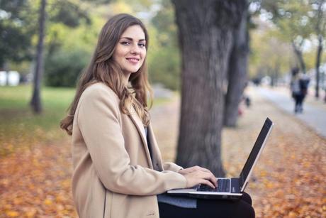 Foto: Andrea Piacquadio at Pexels. Smilende kvinnelig student med laptop i et høstlig utemiljø